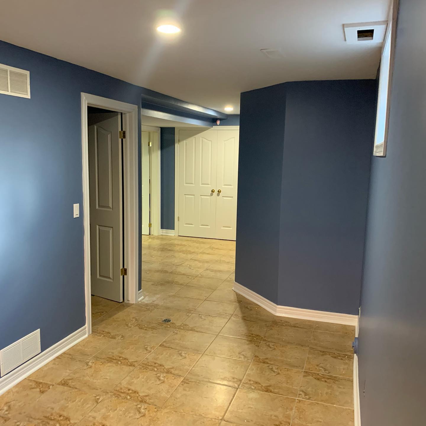Finished basement hallway with tile flooring, painted walls, doors, and recessed lighting