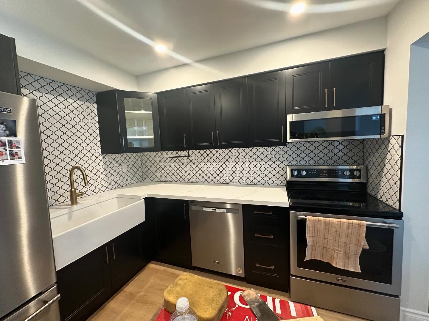 Completed black and white kitchen renovation with cabinetry, counters, backsplash, and appliances